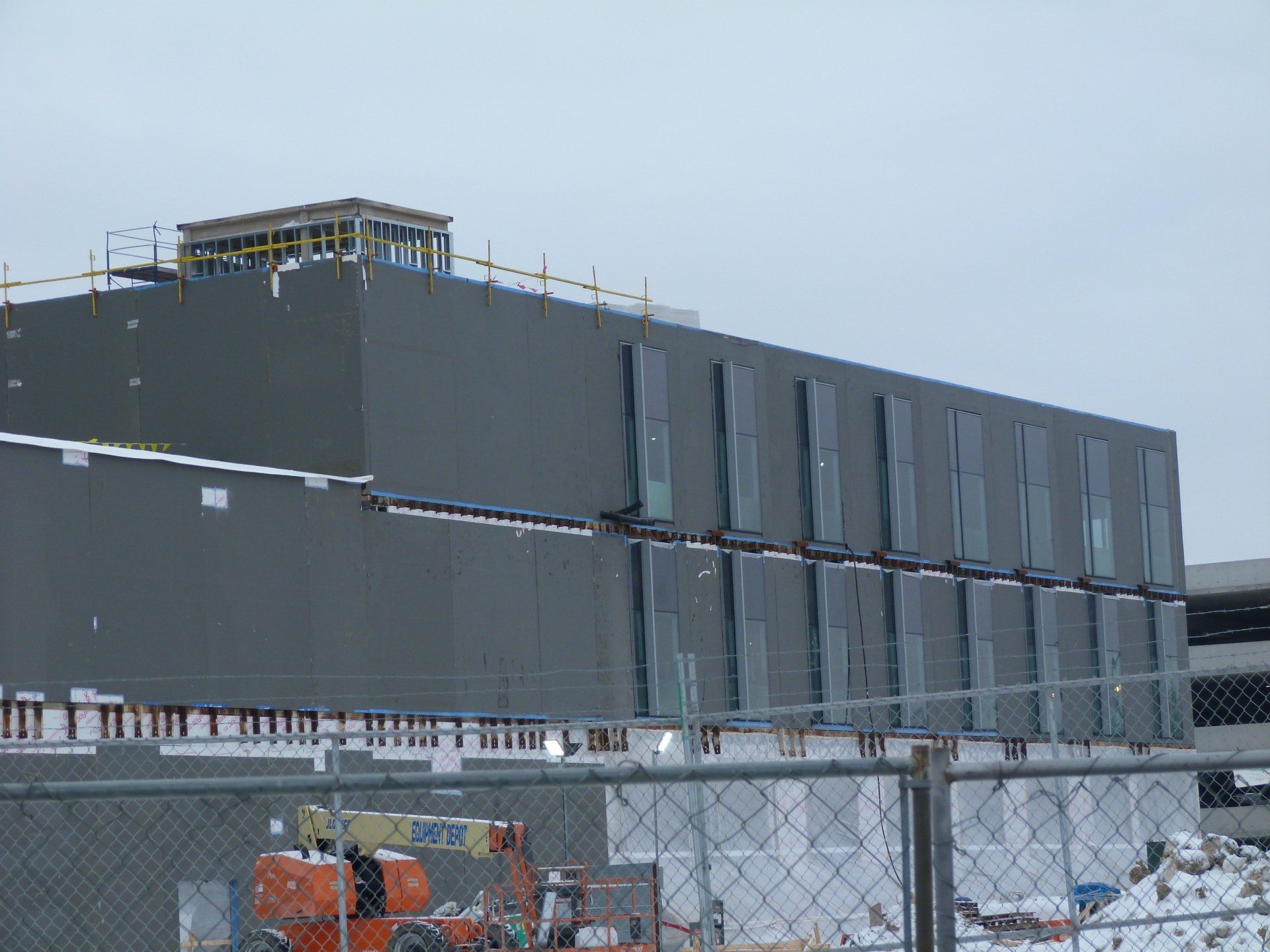 A large building under construction is behind a chain link fence.