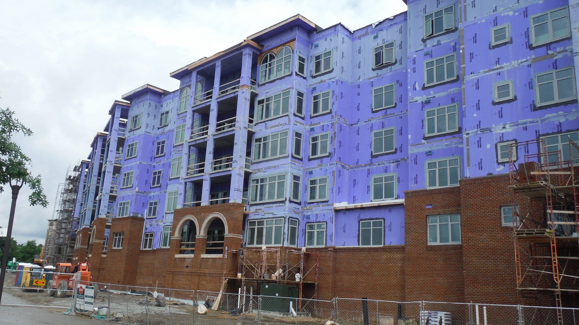 A building with purple insulation panels and many windows is under construction.