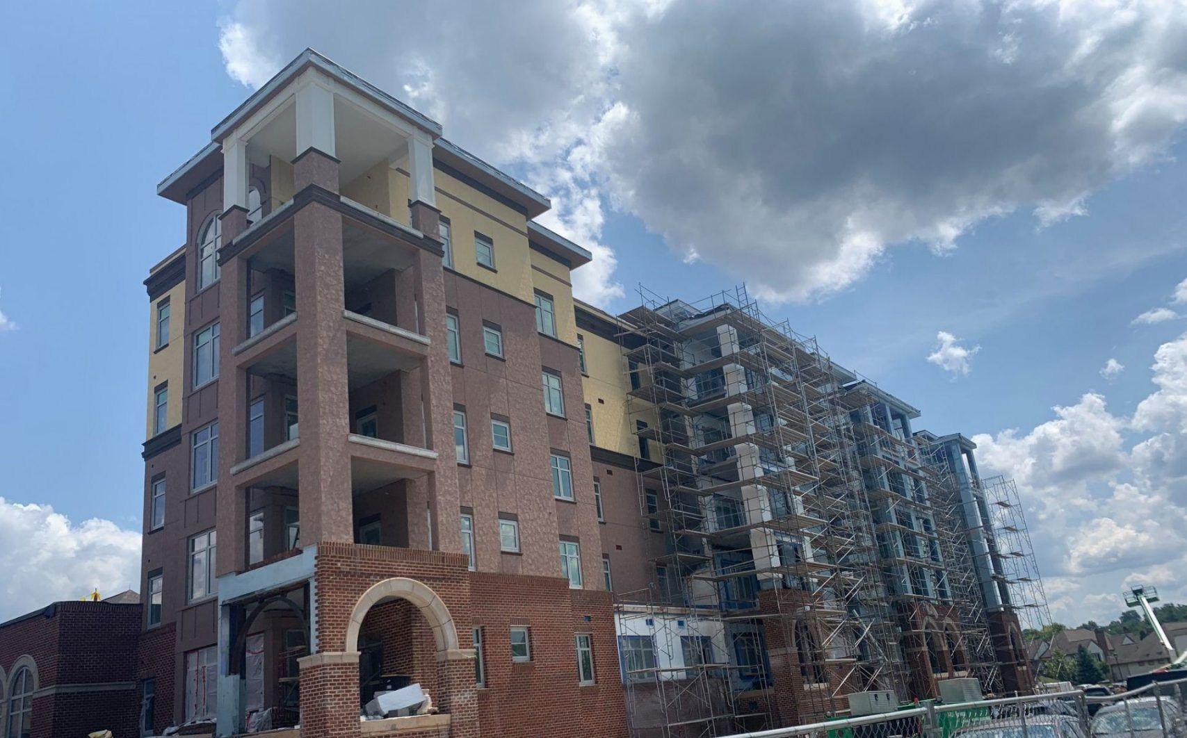 A large brick building under construction with a blue, cloudy sky in the background.