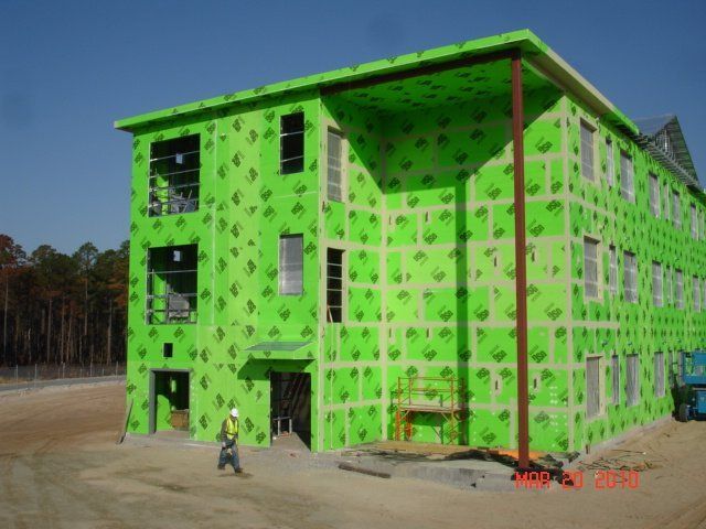 A green building under construction with a man walking in front of it.