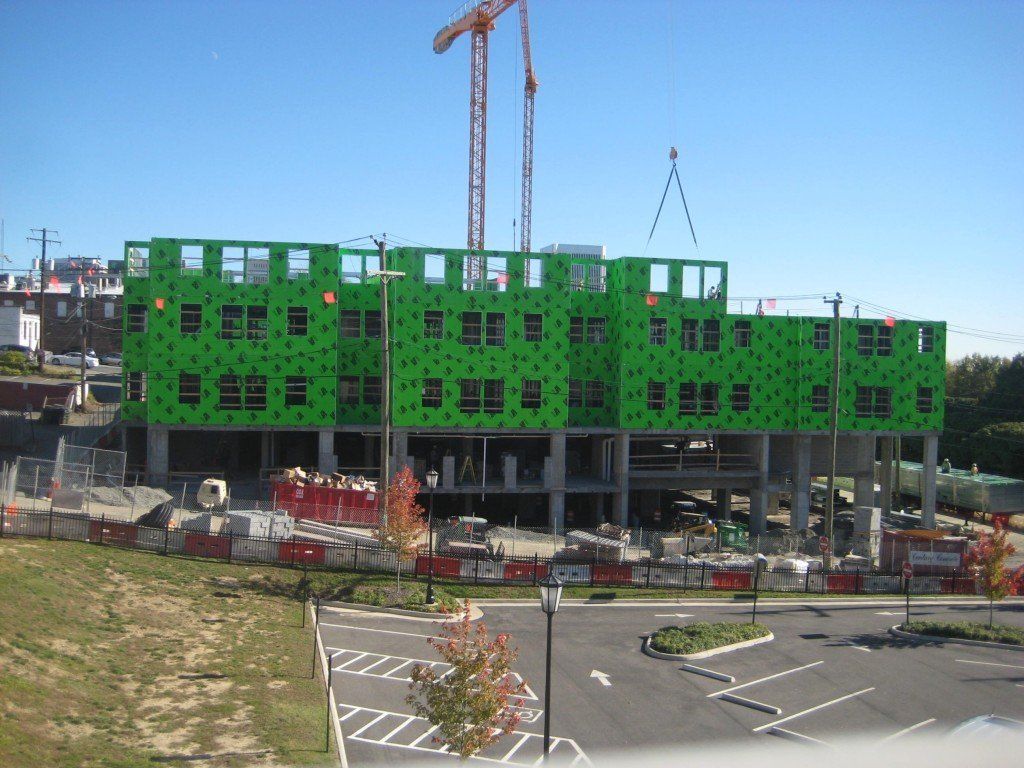 A large green building under construction with a crane in the background.