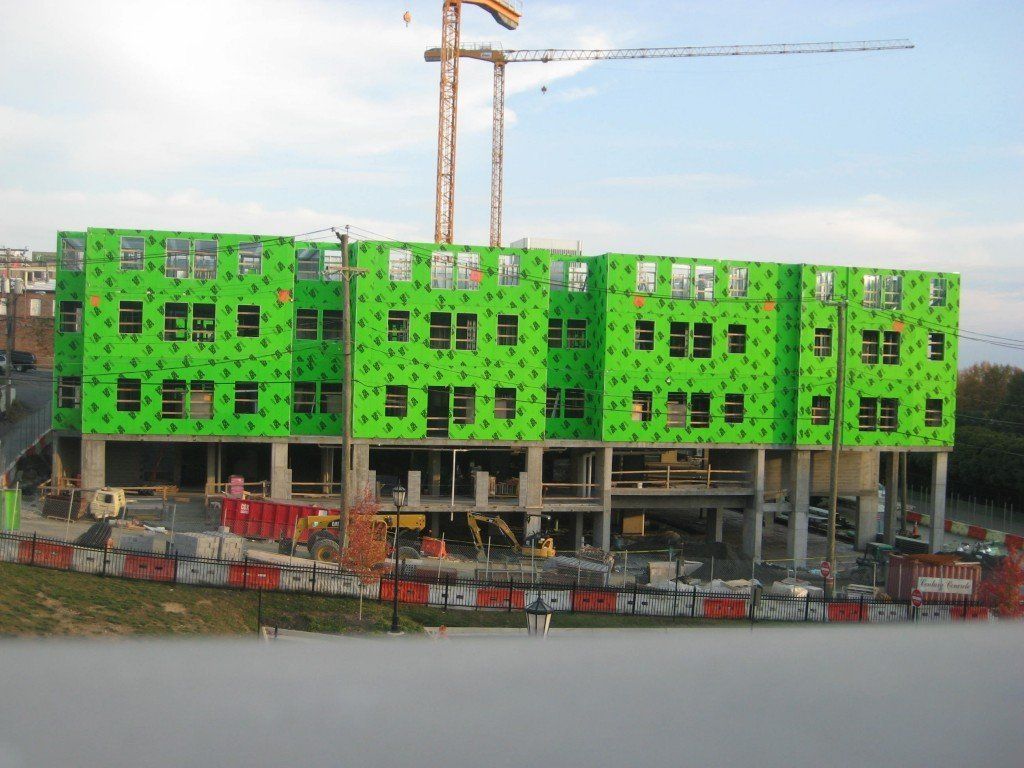 A large green building under construction with a crane in the background