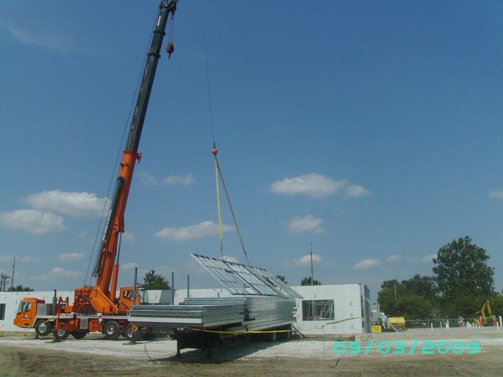 A crane is lifting a piece of metal in front of a building.