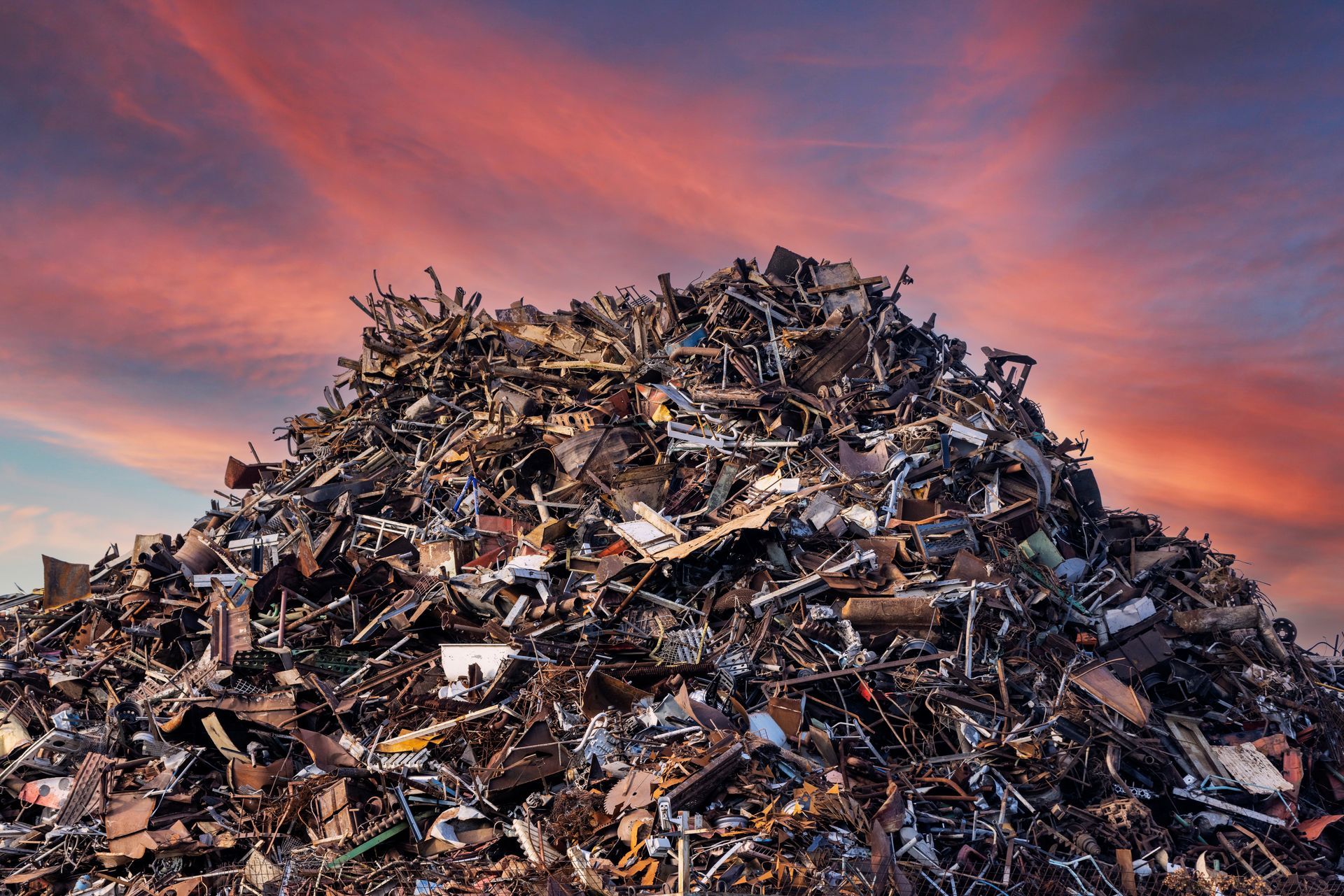 Large pile of scrap metal under a colorful sunset sky.