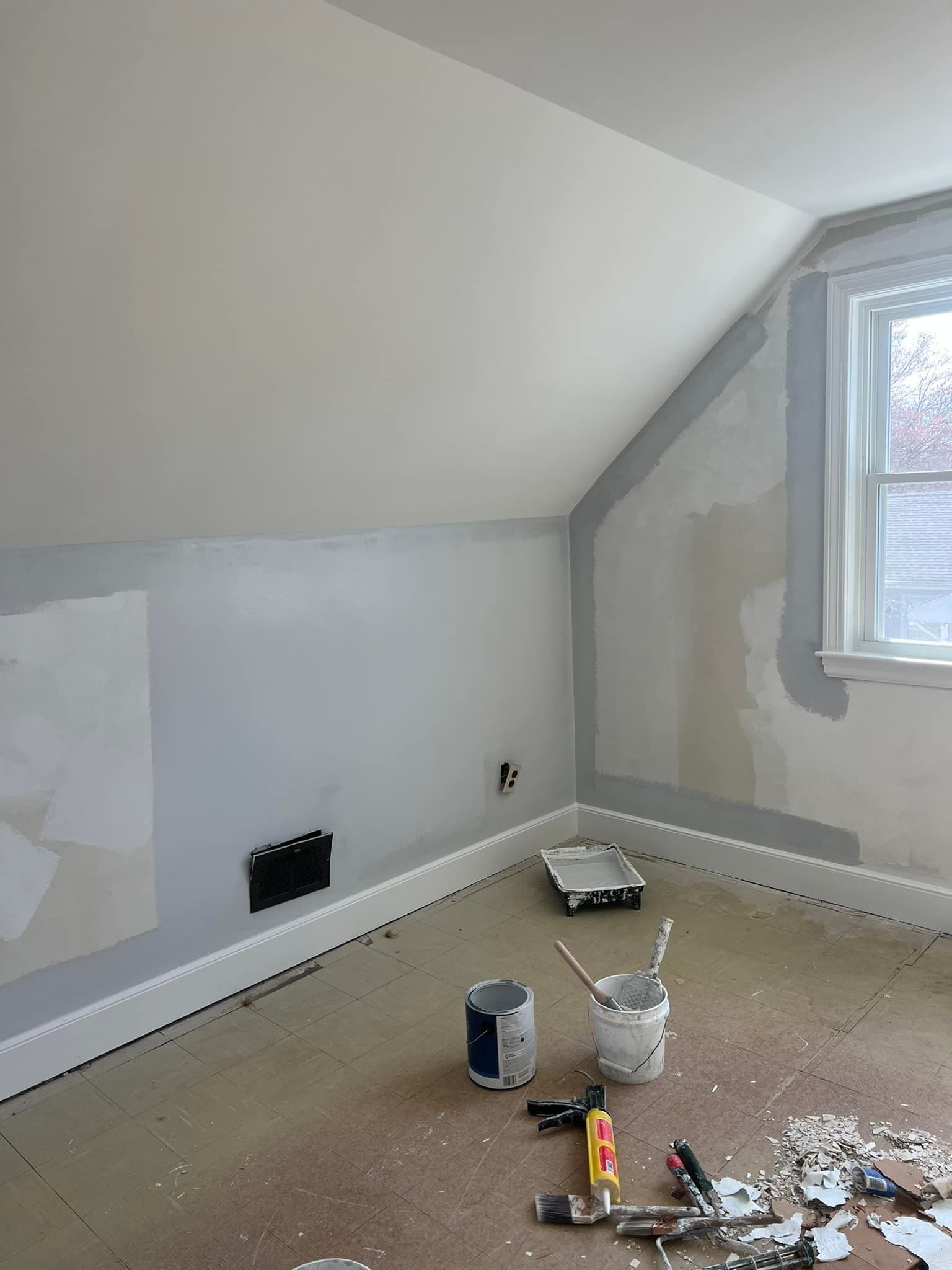 A room with a window and a bucket of paint on the floor.