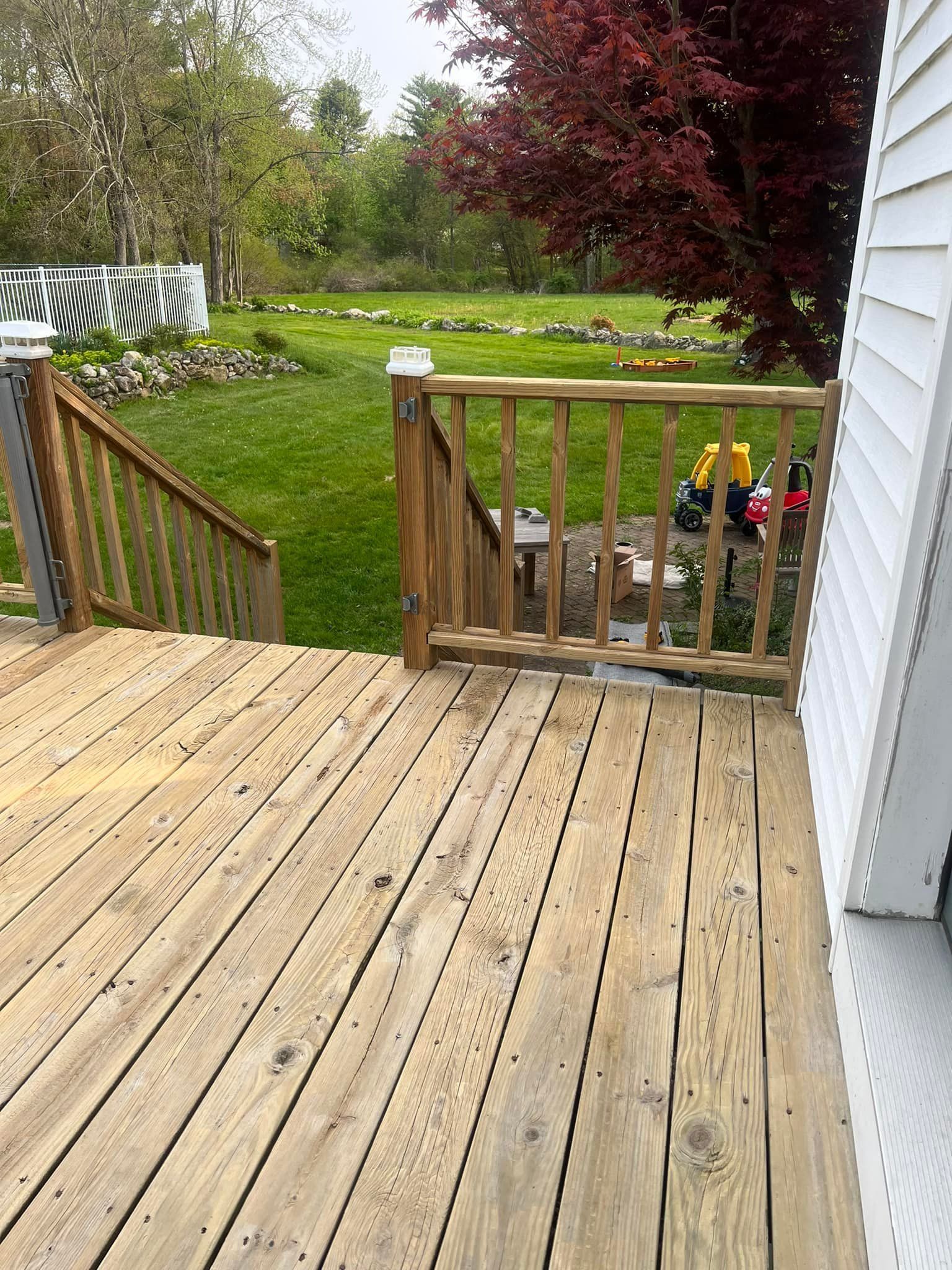 A wooden deck with stairs leading up to it and a white house in the background.