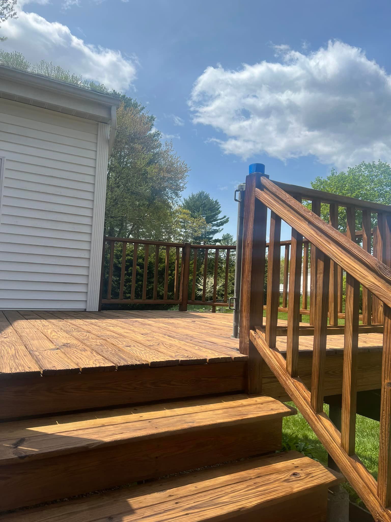 A wooden deck with stairs leading up to it and a white house in the background.