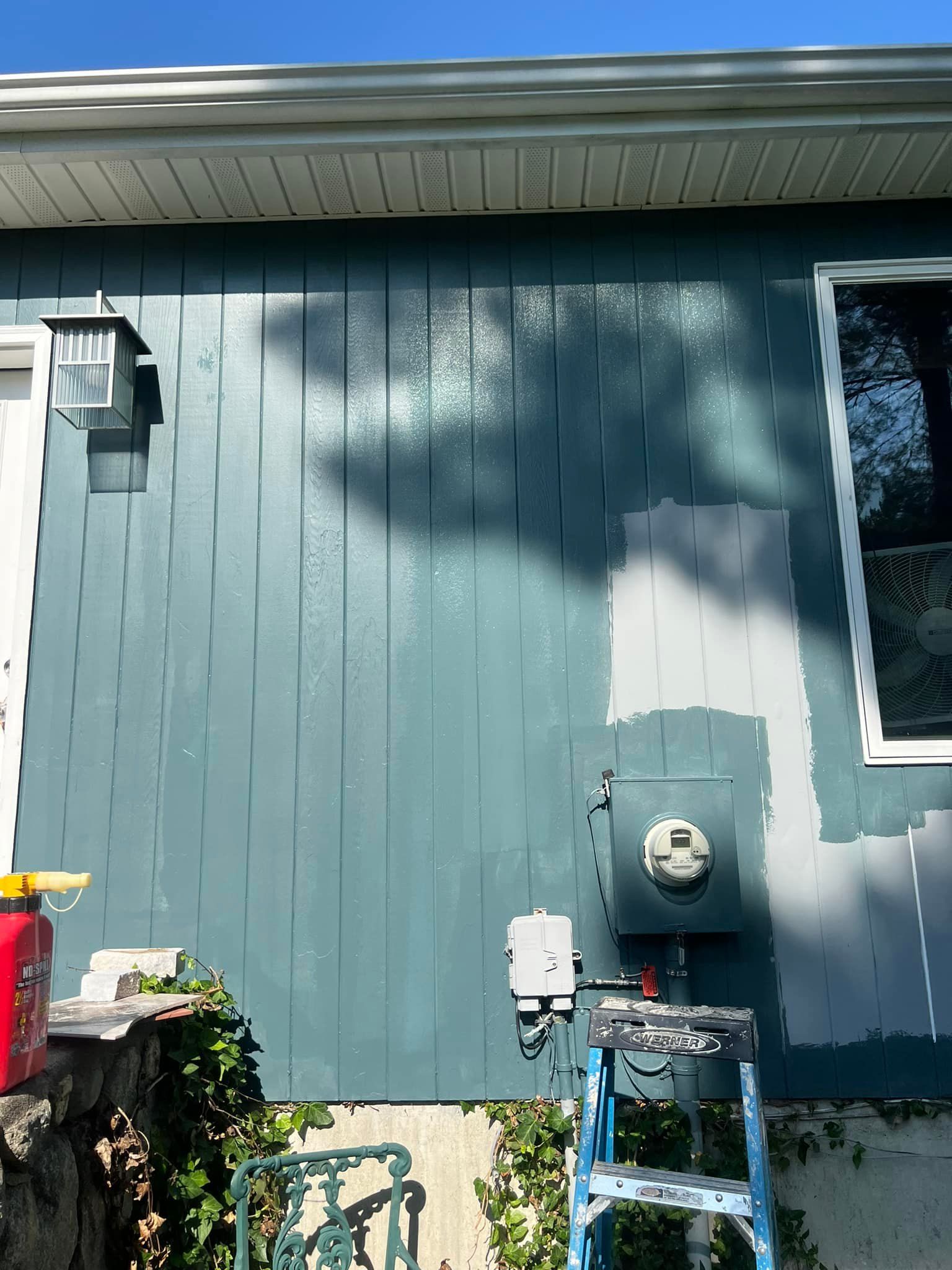 A house is being painted blue and white with a ladder in front of it.