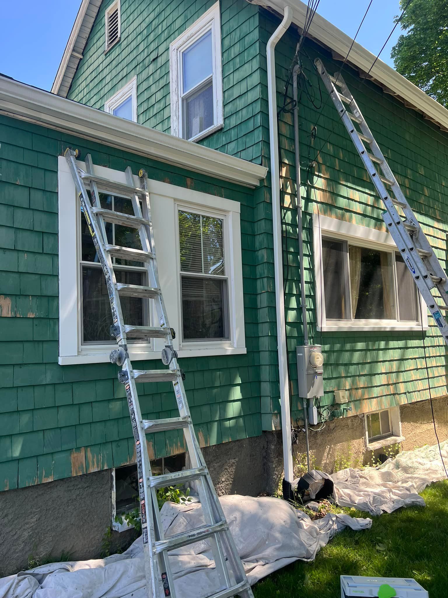 A ladder is sitting on the side of a green house.
