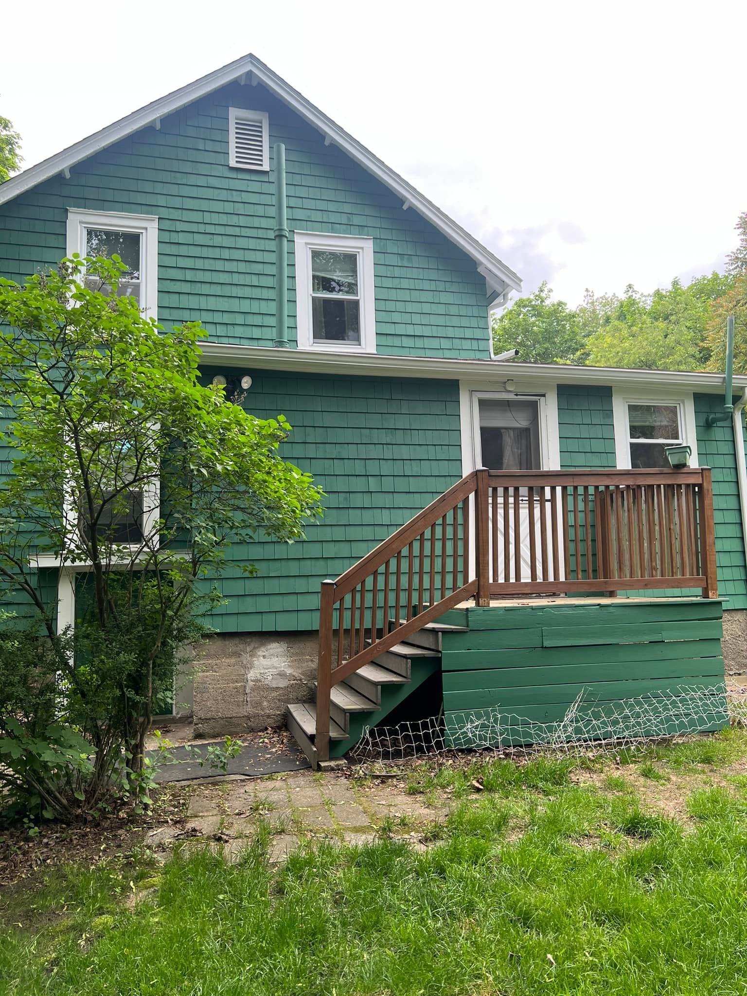 A green house with a wooden deck and stairs.