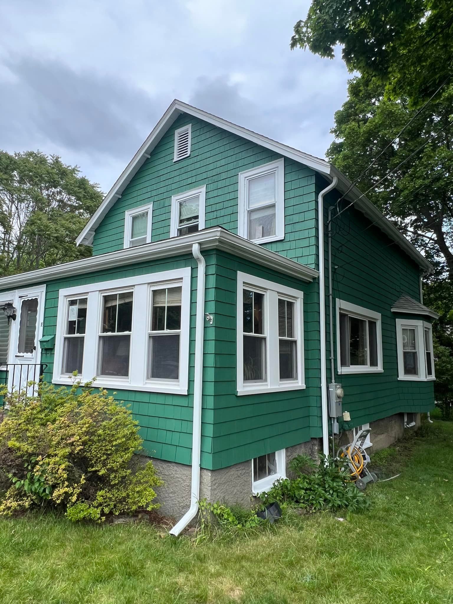 A green house with white trim and windows is sitting in the middle of a lush green field.
