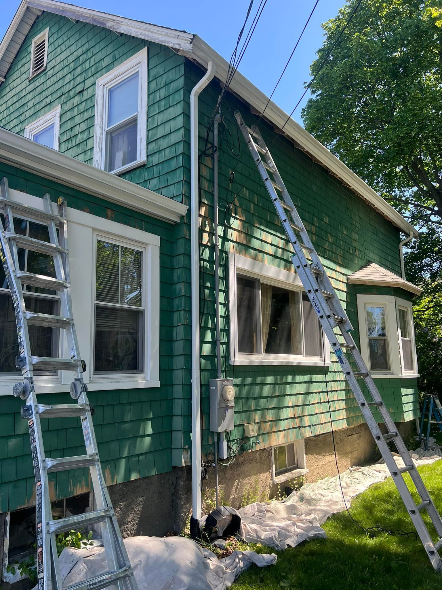 A green house with a ladder leaning against it is being painted.