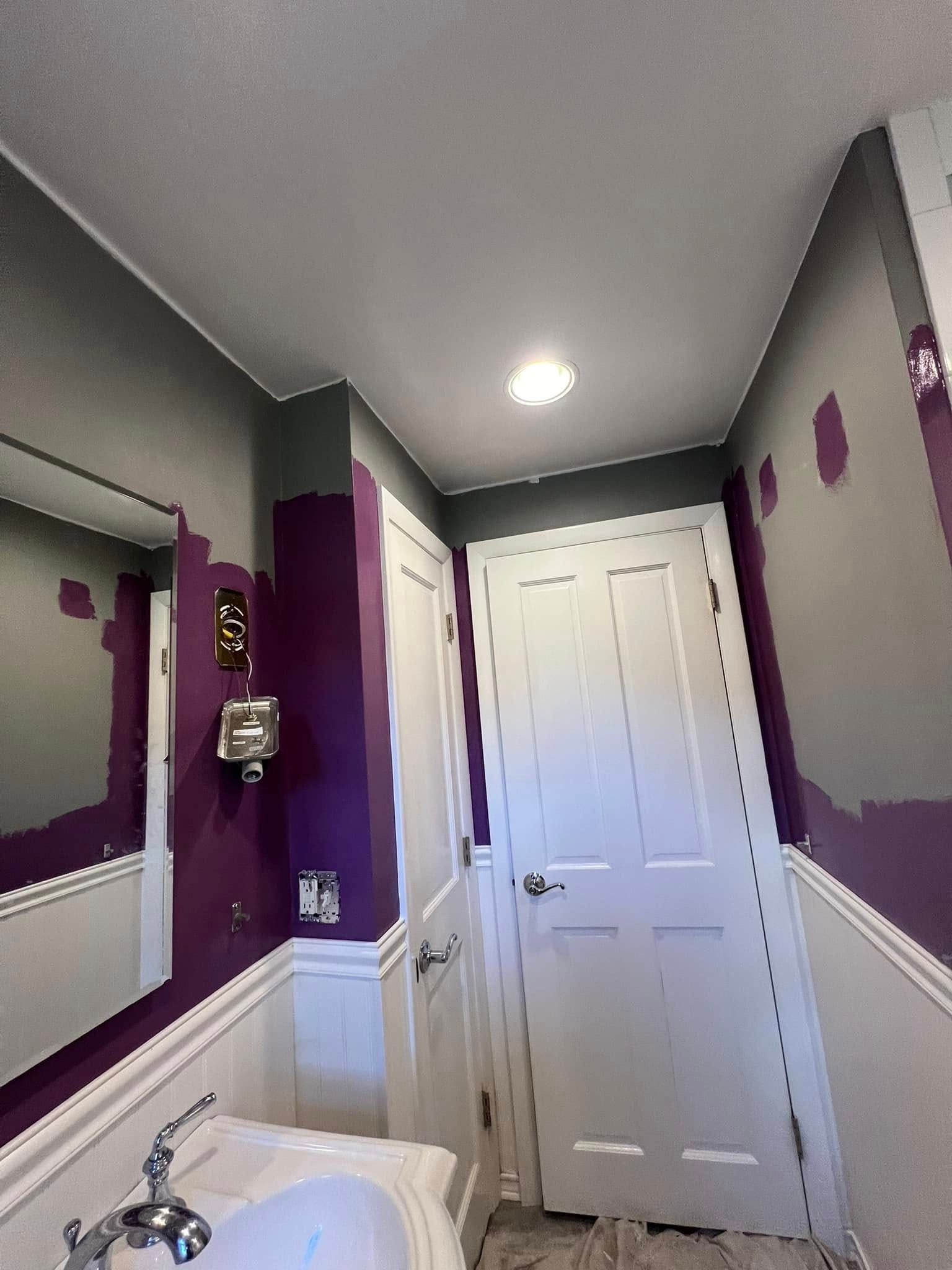 A bathroom with purple walls , a sink , a mirror and a door.