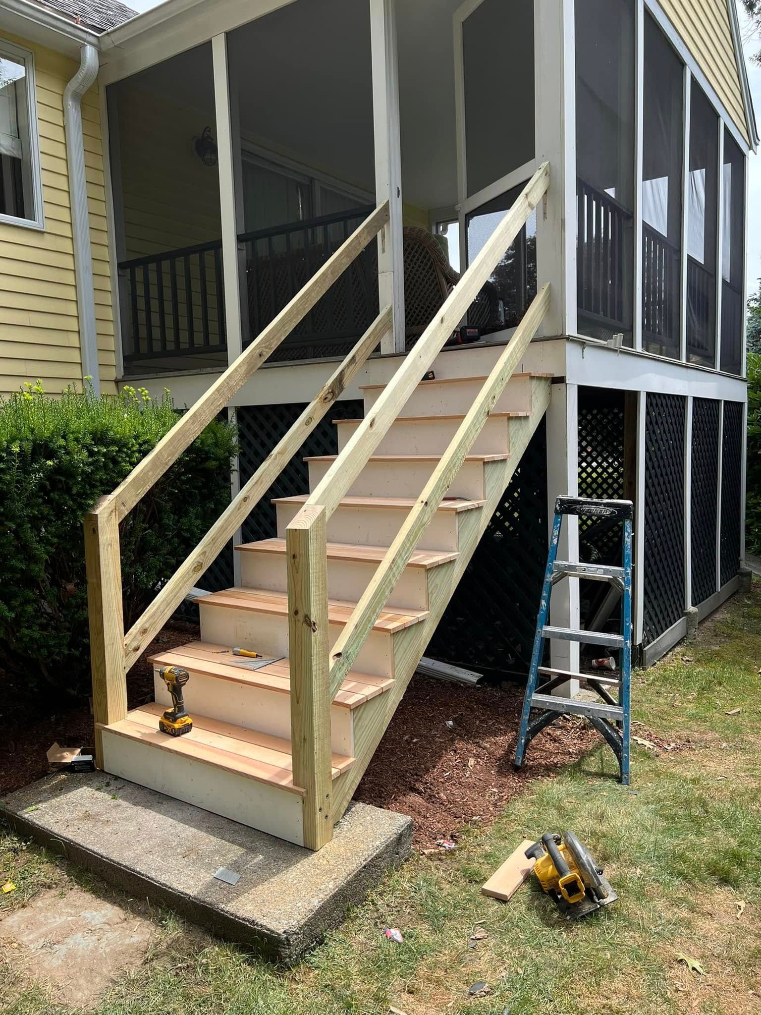A wooden staircase is being built on the side of a screened in porch.