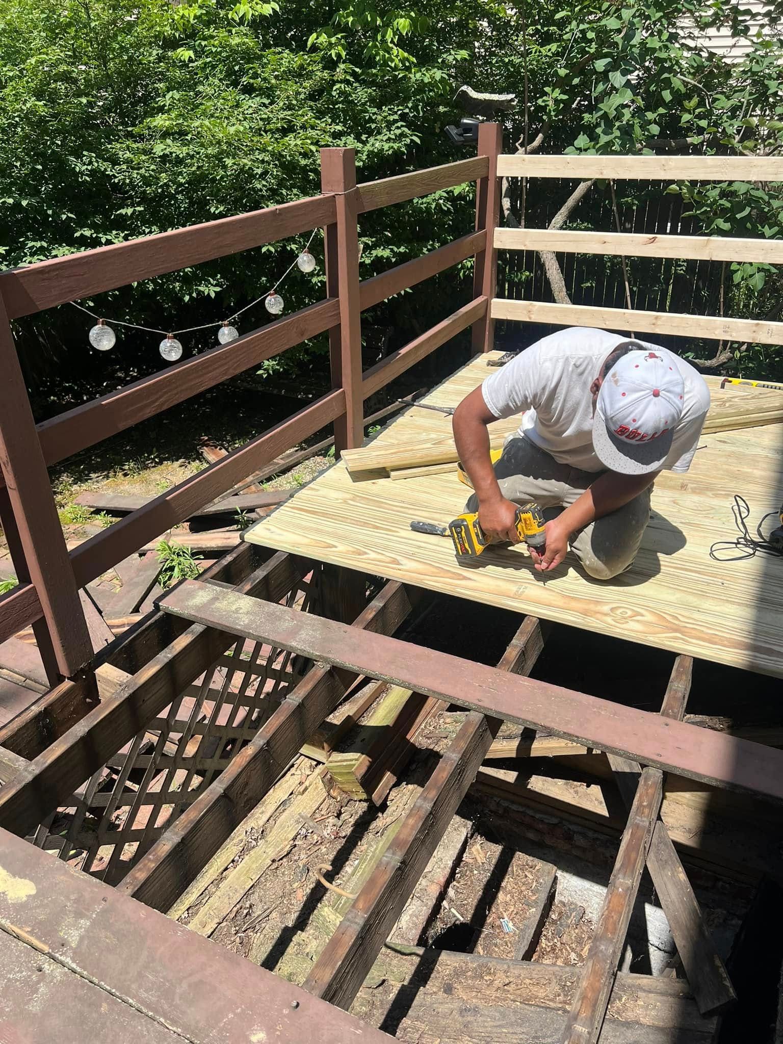 A man is working on a wooden deck with a drill.