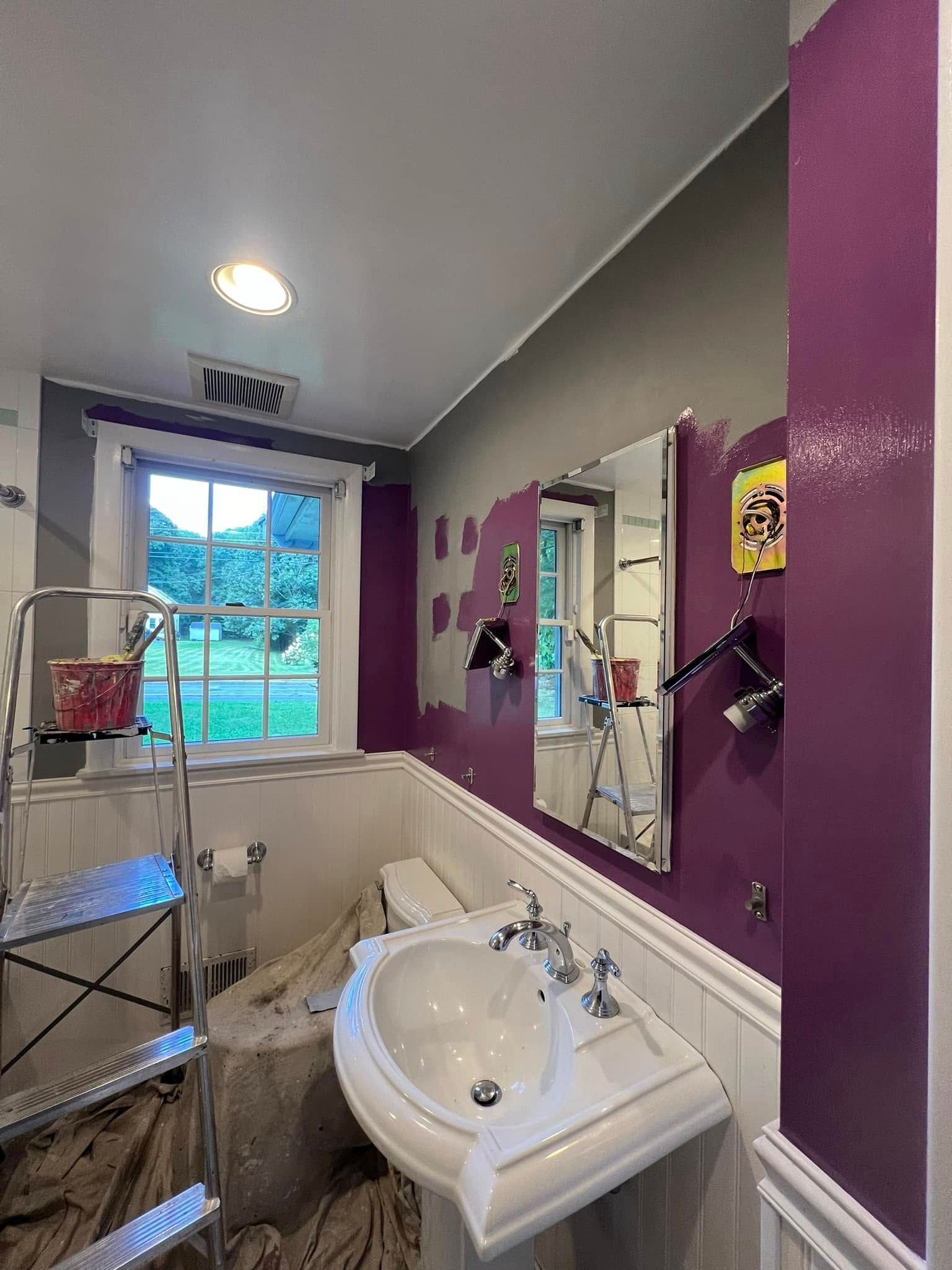 A bathroom with purple walls , a sink , toilet and mirror.