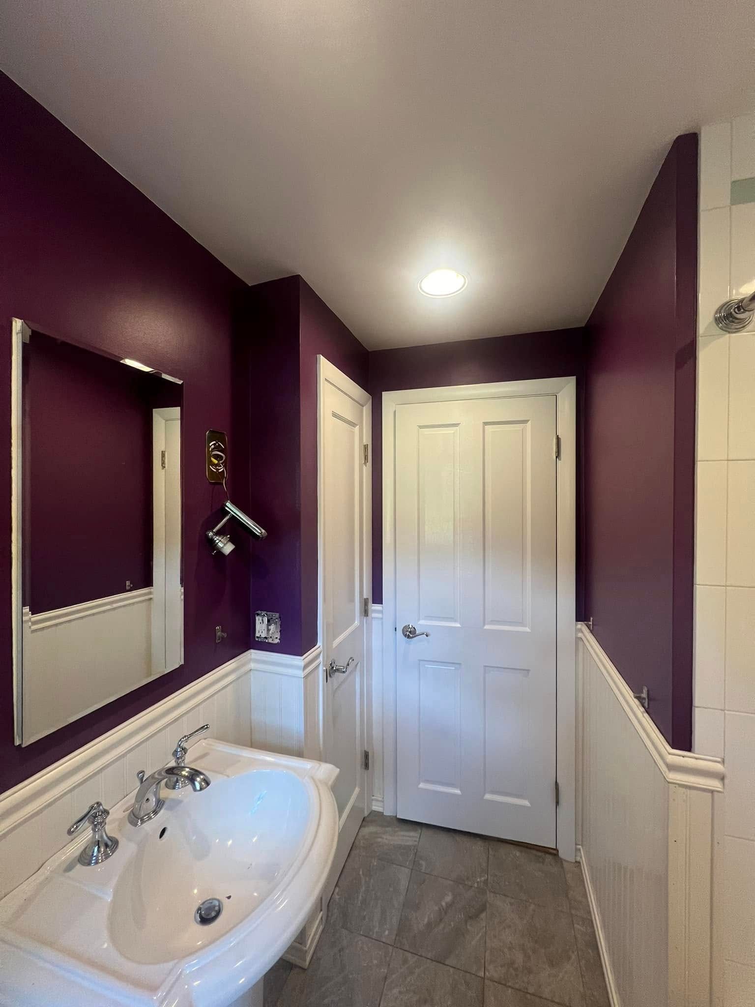A bathroom with purple walls and a sink and mirror
