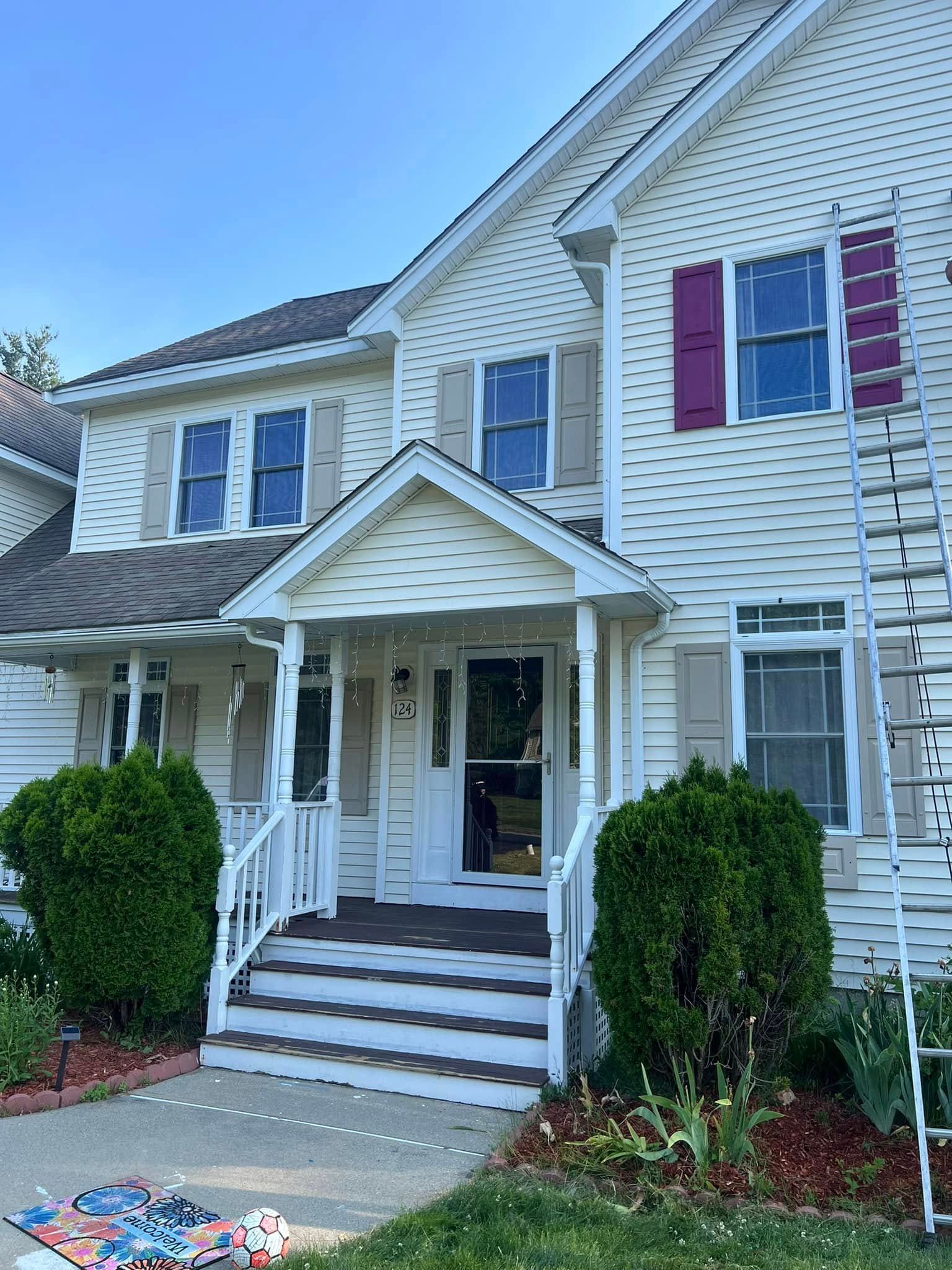 A white house with red shutters and a ladder in front of it.