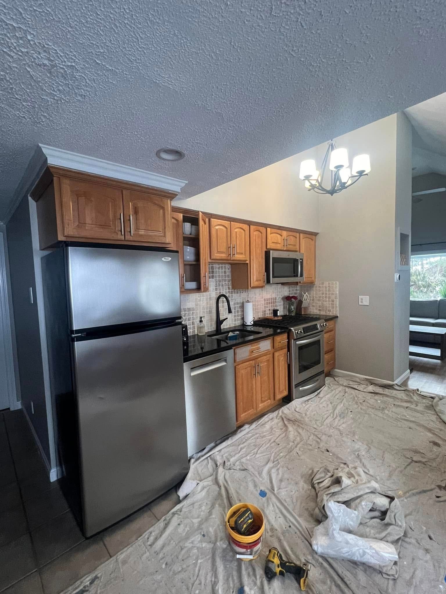 A kitchen with stainless steel appliances and wooden cabinets is being painted.