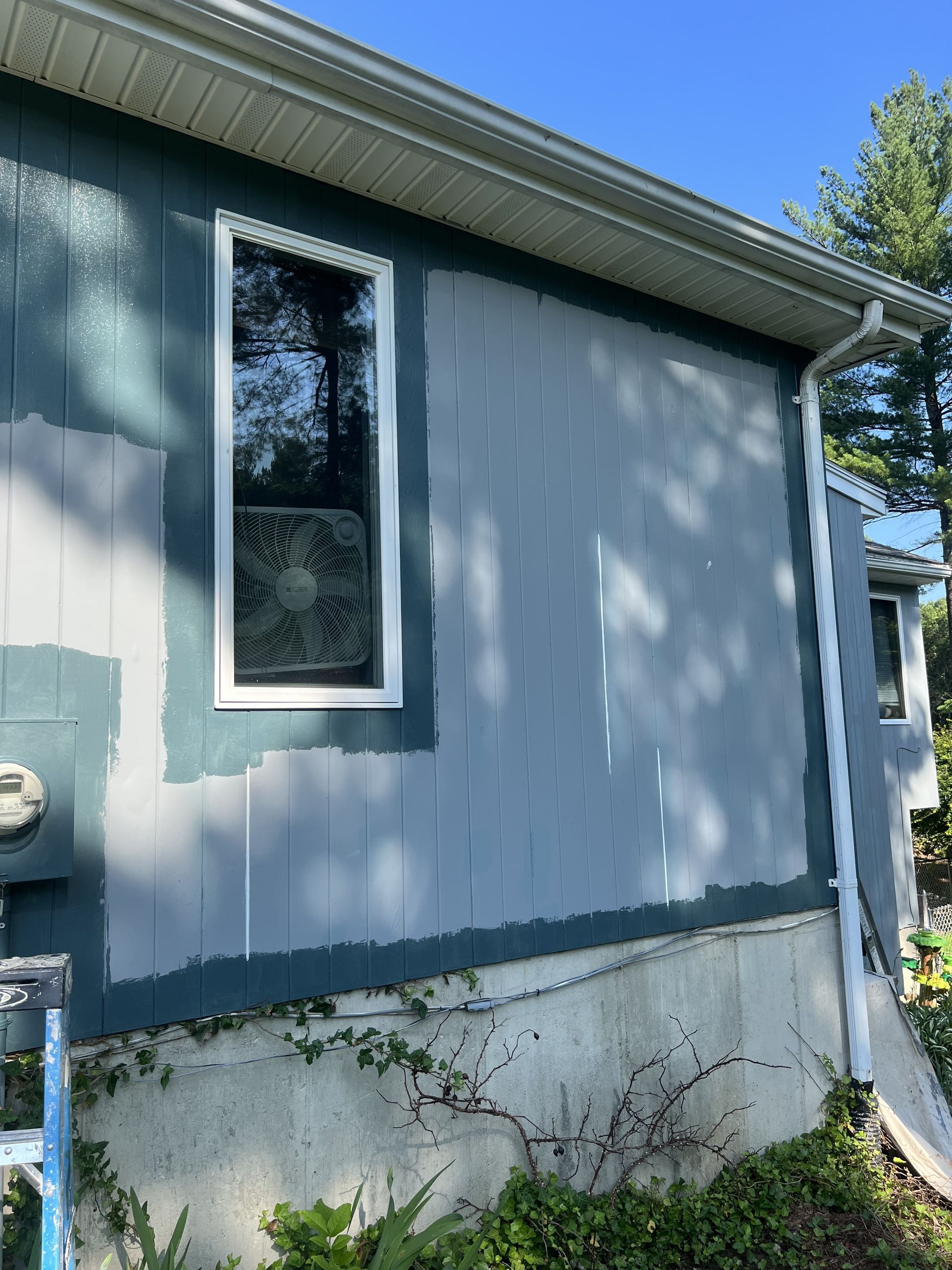 A blue house with a white window is being painted.