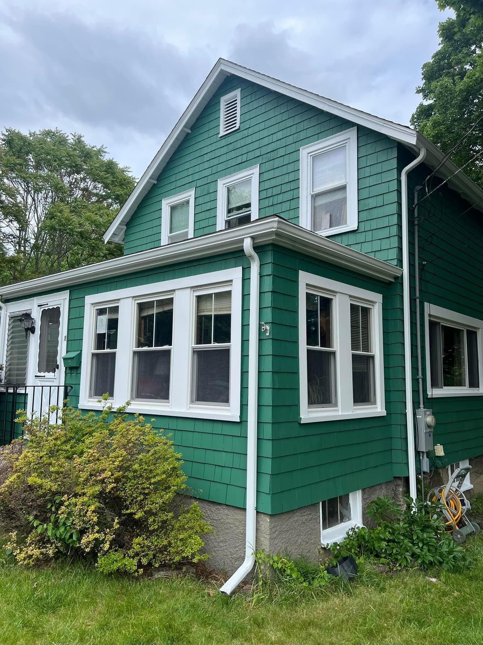 A green house with white trim and windows is sitting on top of a lush green field.
