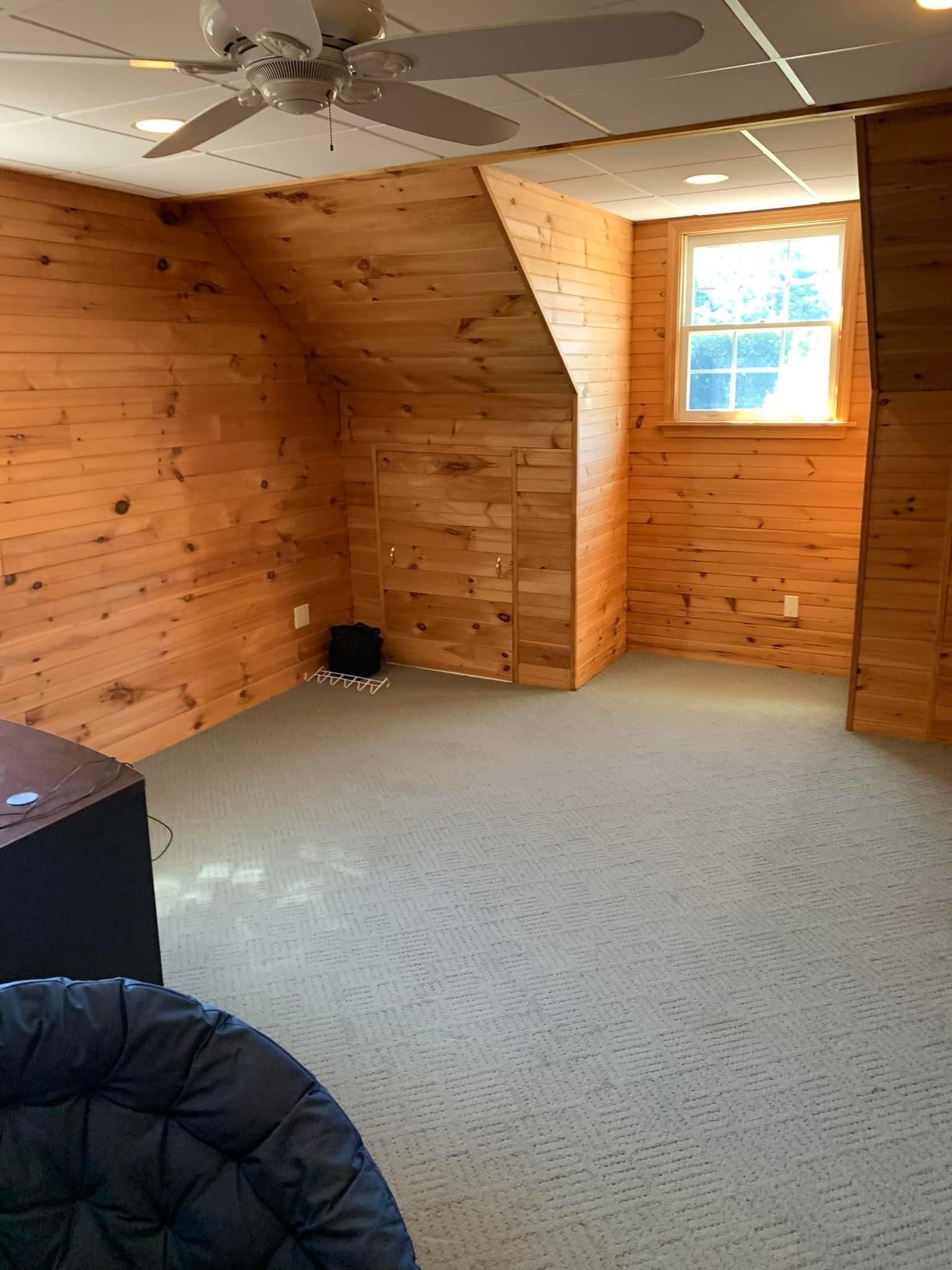 An empty room with wood paneling and a ceiling fan.