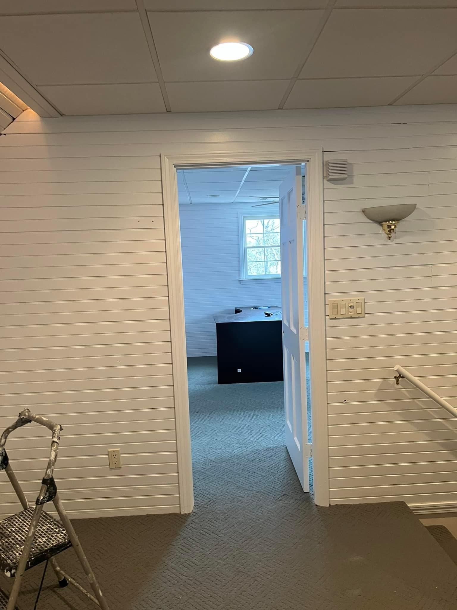 A hallway with a ladder and a door leading to a bathroom.