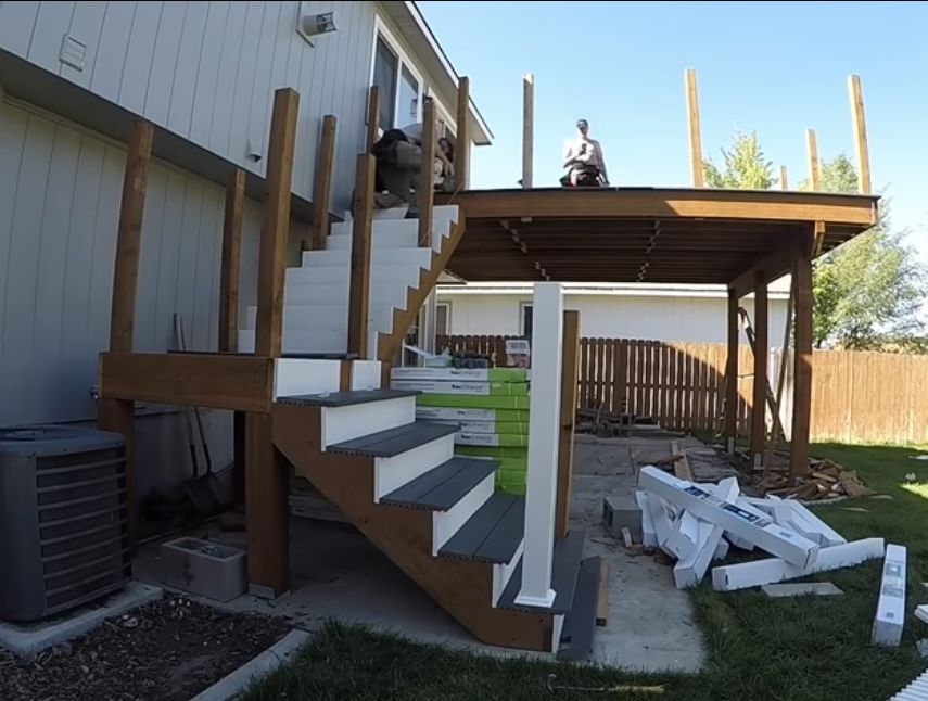A man is sitting on top of a wooden deck with stairs