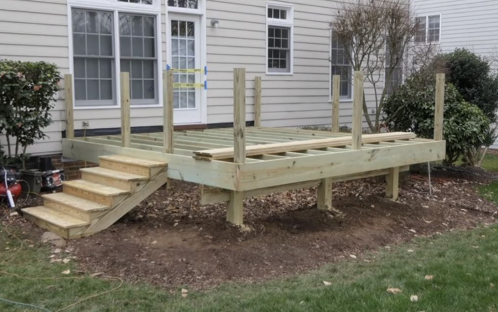 A wooden deck with stairs is being built in front of a house.