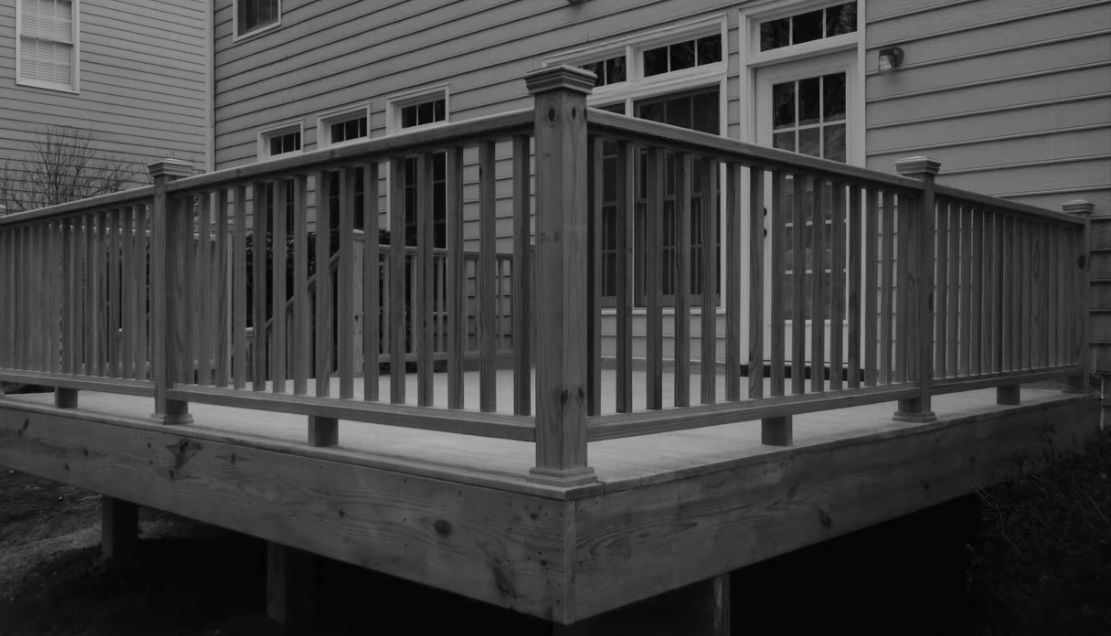 A black and white photo of a wooden deck in front of a house.