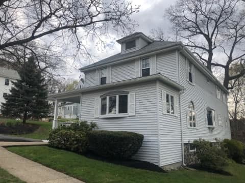 A white house with a gray roof is sitting on top of a lush green hillside.