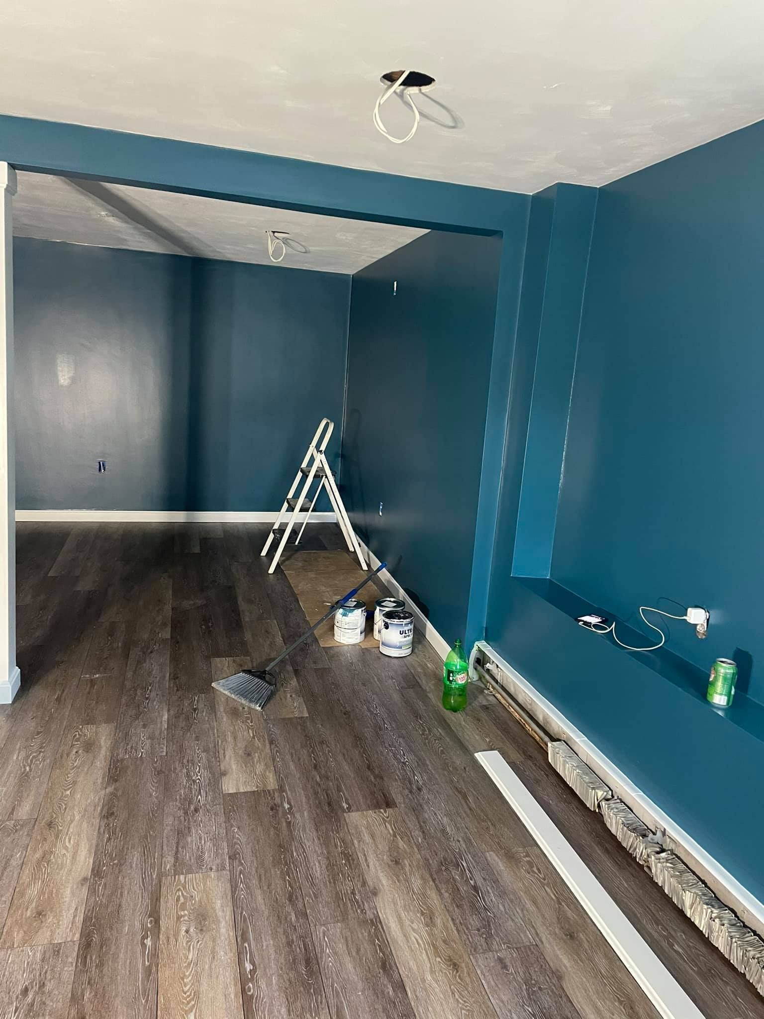 A room with blue walls and wooden floors is being painted.