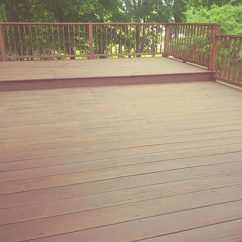 An empty wooden deck with a railing and trees in the background