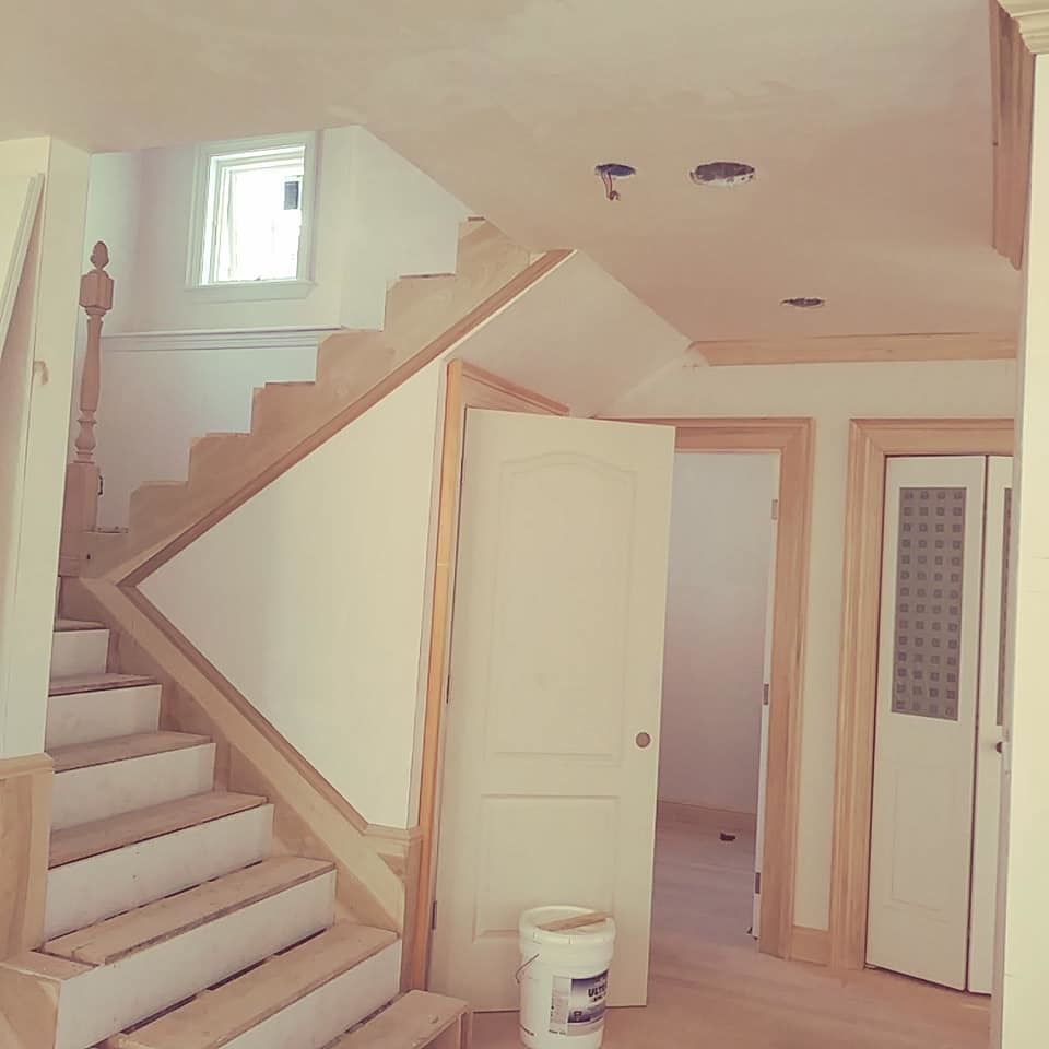 A bucket of paint sits in a hallway next to a staircase