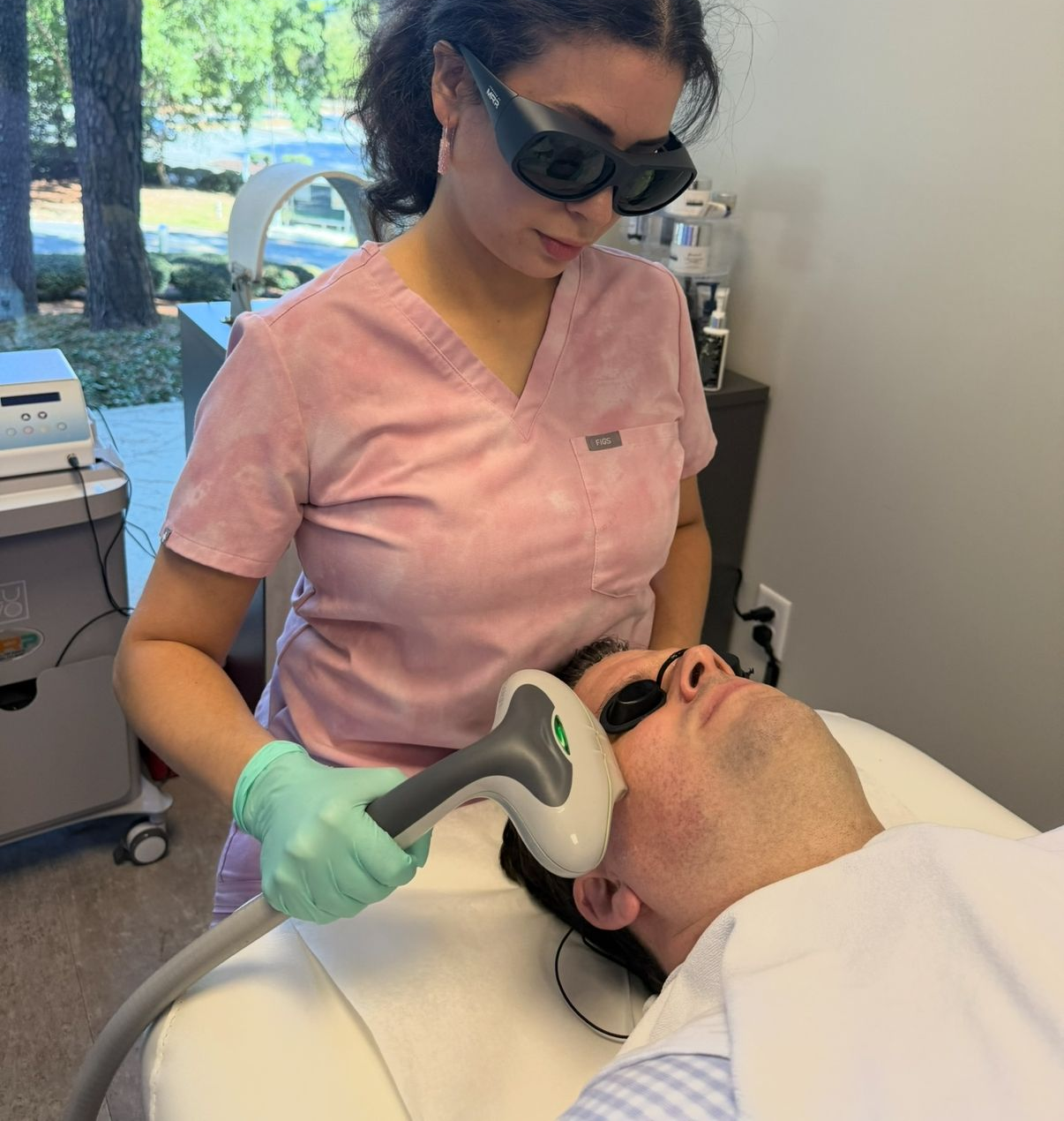Woman receiving laser skin treatment on face, wearing protective eyewear in a medical setting.