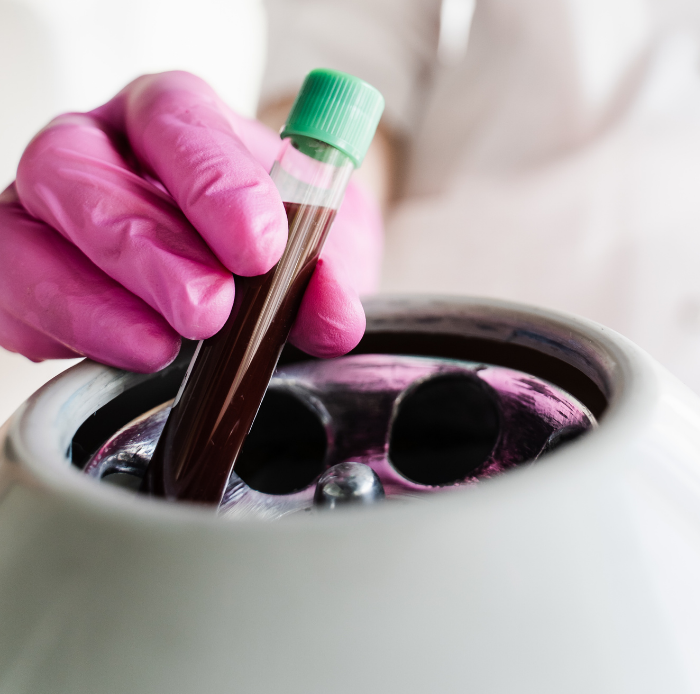 Woman in white robe looking in a hand mirror, touching her neck, smiling in a bright bathroom.