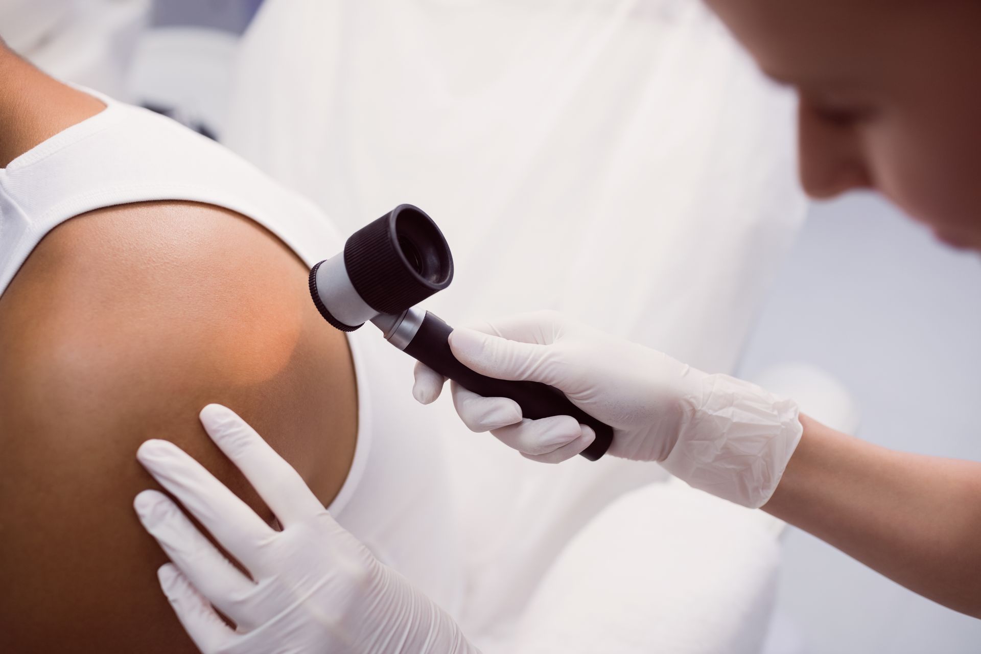 Doctor examining a mole on a woman's back in a medical office.