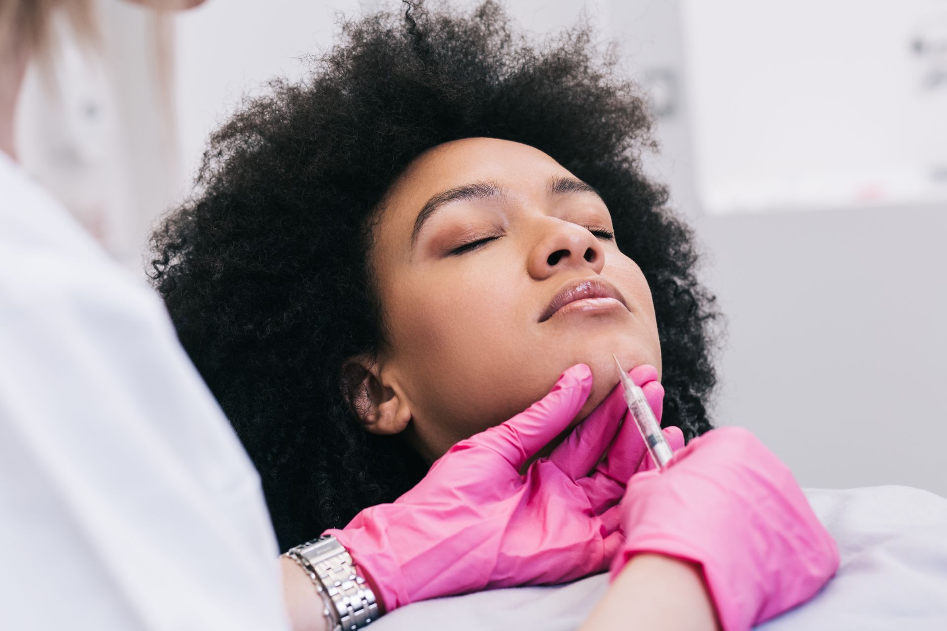 Woman receiving cosmetic injection in chin, gloved hands hold syringe.