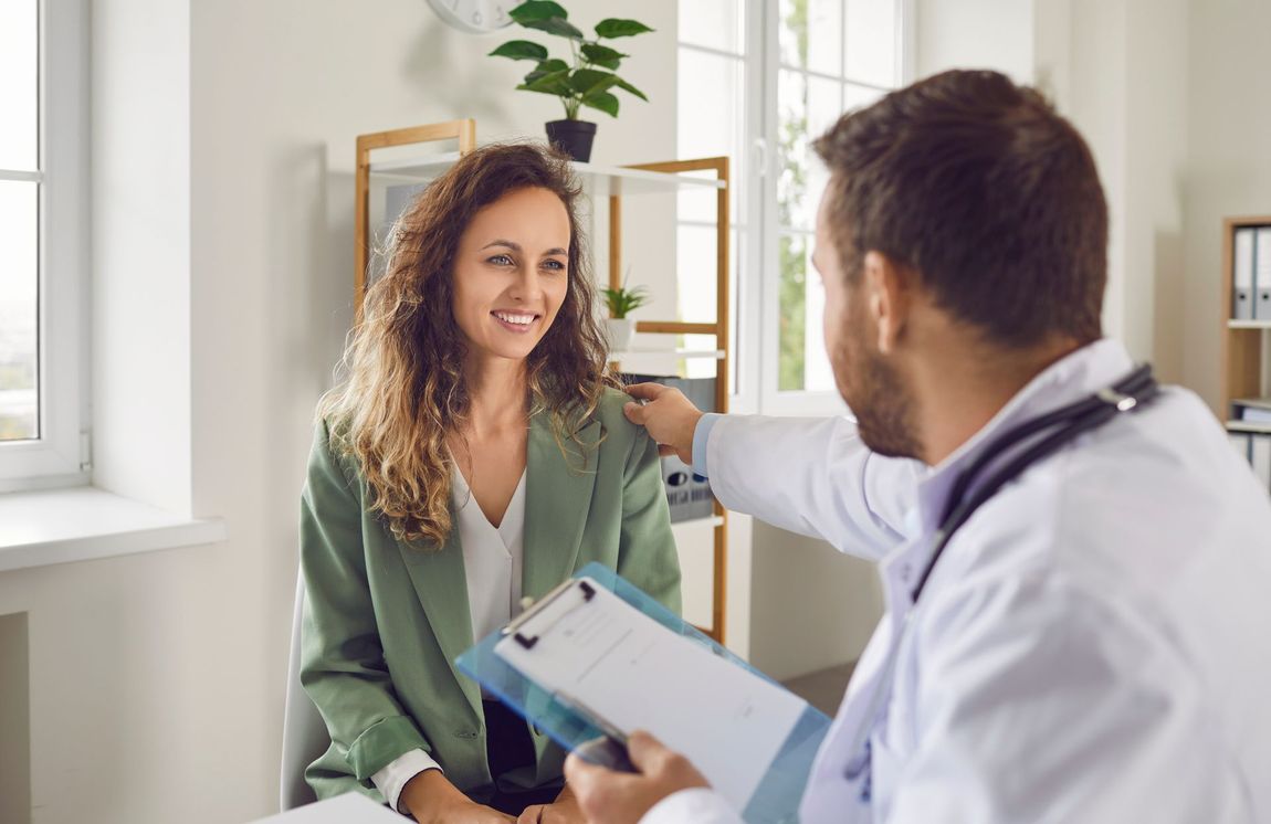 Doctor consulting with a smiling patient in a bright clinic, holding a clipboard.