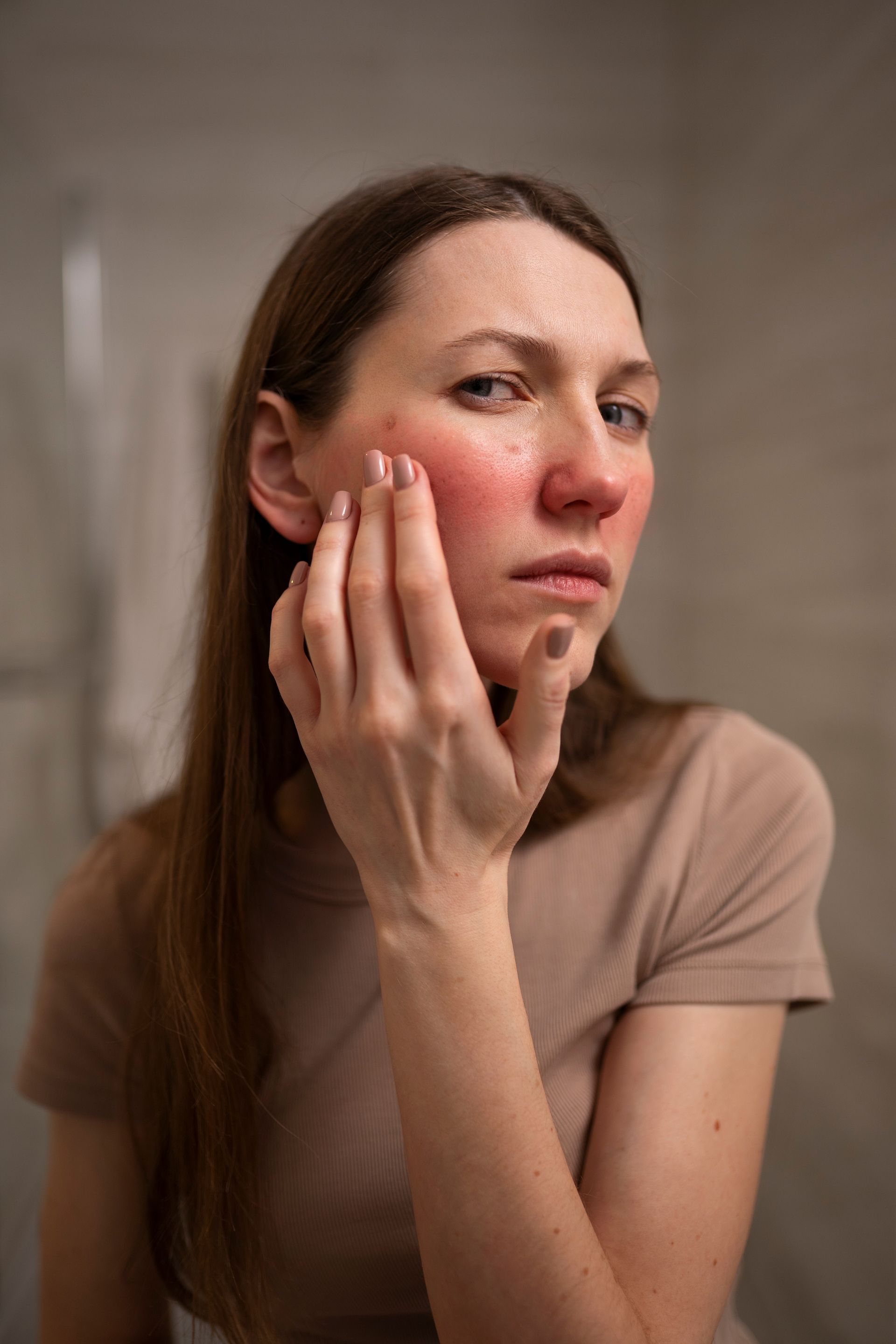 Woman with red skin on her face and a concerned expression, touching her cheek in a bathroom.