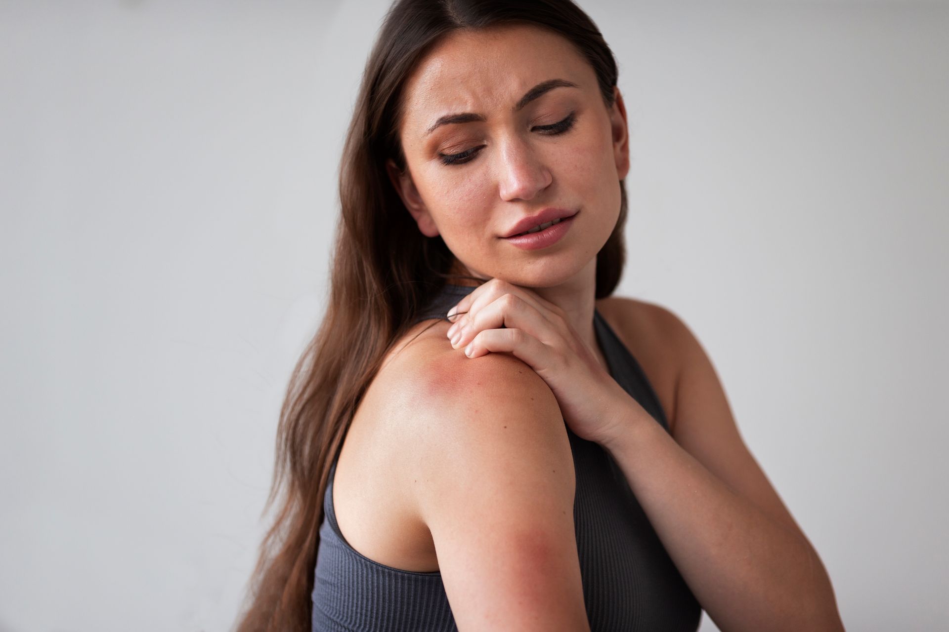 Woman touching her red shoulder; appears to be in pain against a plain white background.