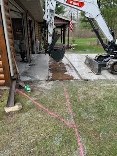 A bobcat excavator is digging a hole in the ground in front of a house.