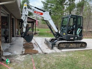 A small excavator is sitting in a driveway next to a house.