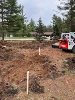 A bobcat is driving through a dirt field next to a house.
