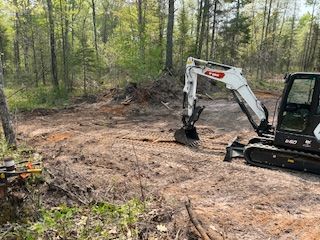 A small excavator is digging a hole in the middle of a forest.