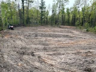 A tractor is driving through a muddy field in the woods.