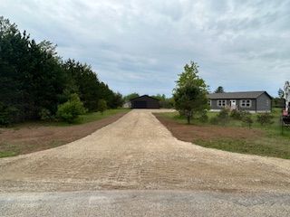 A dirt road leading to a house in the middle of a field.