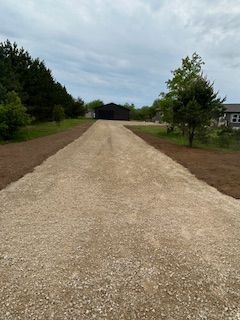 A gravel driveway leading to a shed in the middle of a field.