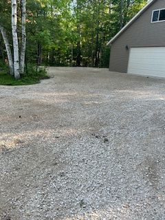 A gravel driveway leading to a garage with trees in the background.