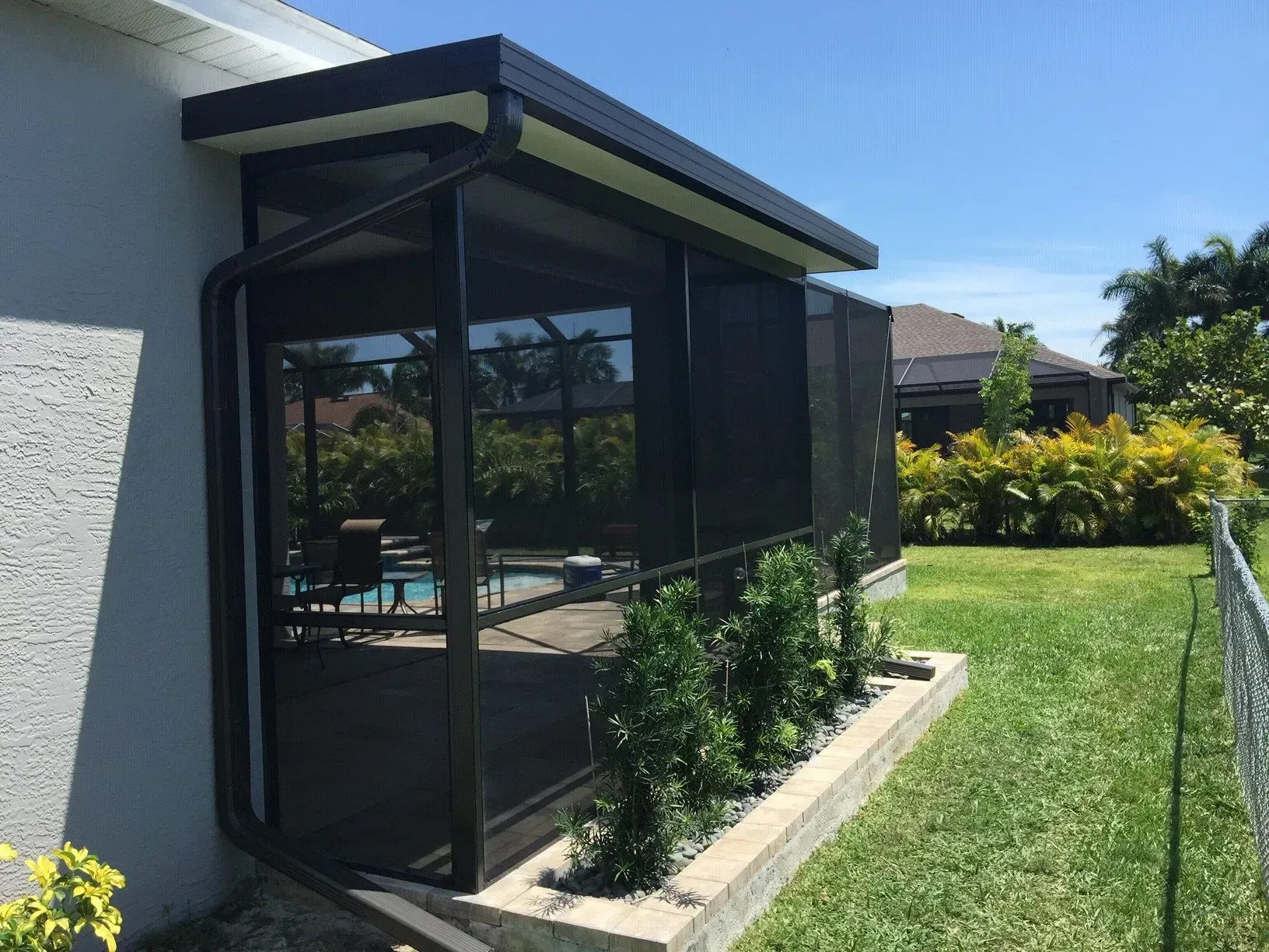 A screened in porch next to a house with a pool.